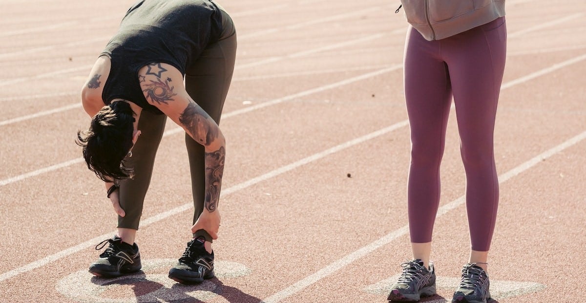 Two sportswomen stretching body before running in a stadium