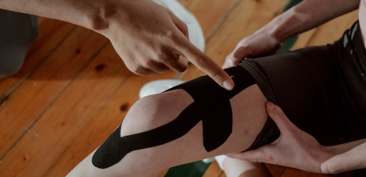 Person Putting a Kinesio Tape on another Person's Knee

