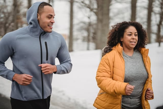A woman with a trainer during running workout in a snowy park

