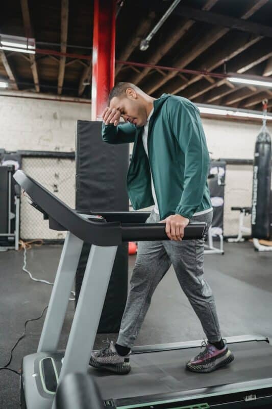 Tired man walking on treadmill in gym
