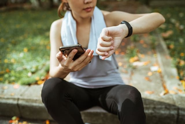 A female runner sitting on a bench with a phone on her hand 