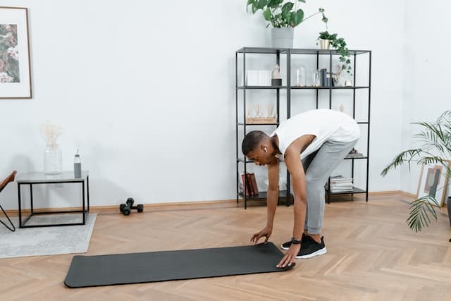 Man putting the Yoga Mat on a Wooden Floor
